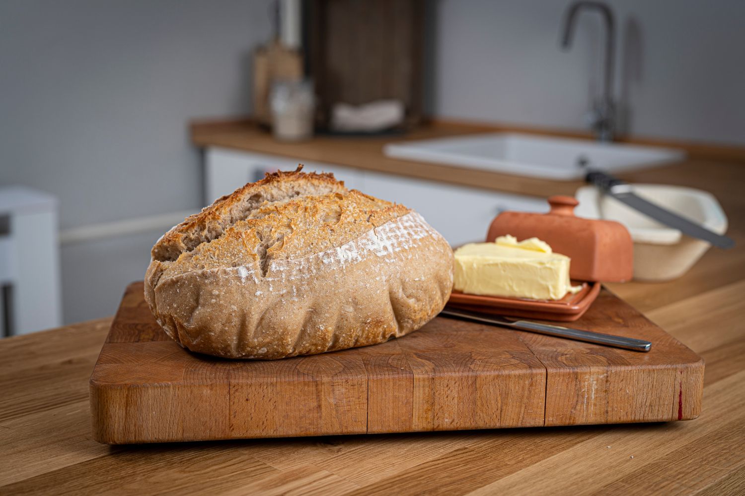 Ein Laib Brot und ein Butterstück auf einem Holzbrett in einer Küche.