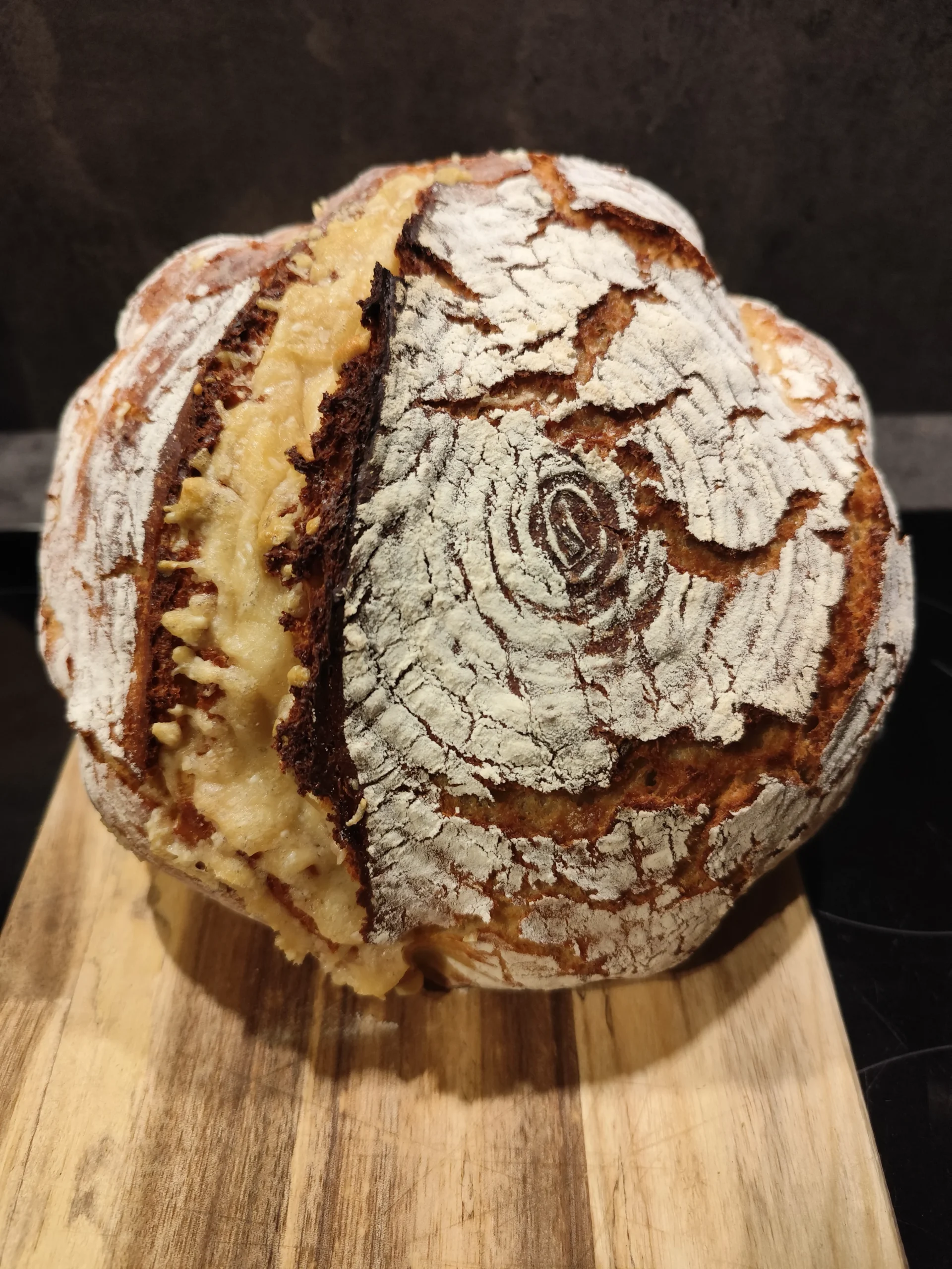 Krustenbrot mit aufgerissener Kruste auf einem Holzbrett, mit goldbrauner Oberfläche und Mehl bestäubt.