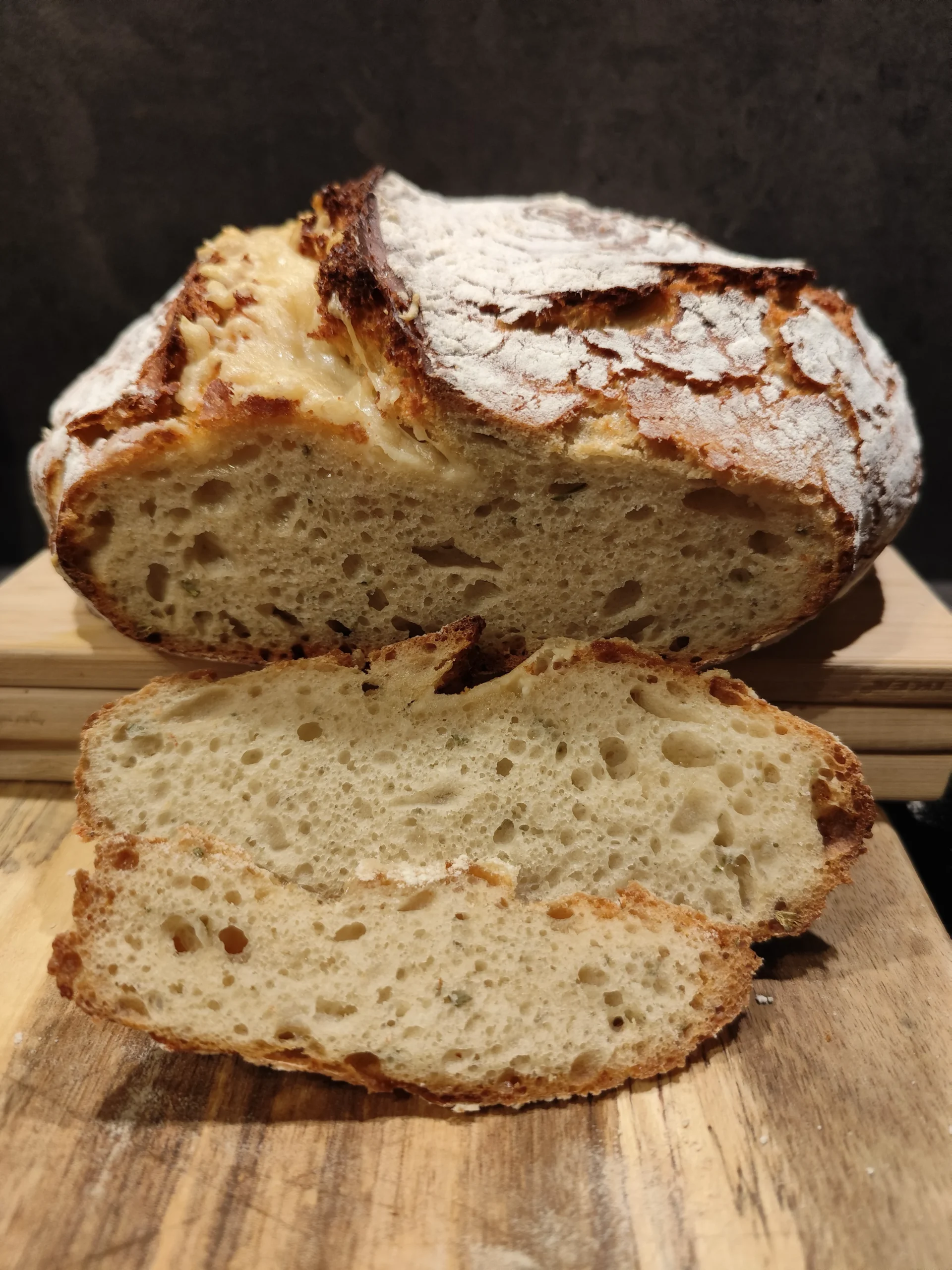 Aufgeschnittenes Sauerteigbrot auf einem Holzbrett, knusprige Kruste und luftige Krume sichtbar.