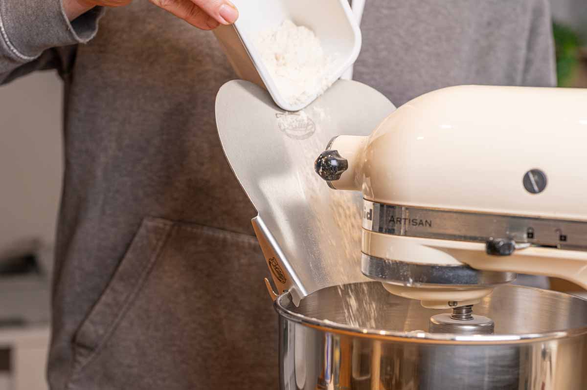 Herzschütte Einfüllhilfe am Rand einer Edelstahl-Rührschüssel montiert beim Einfüllen von Wasser in einen Brotteig