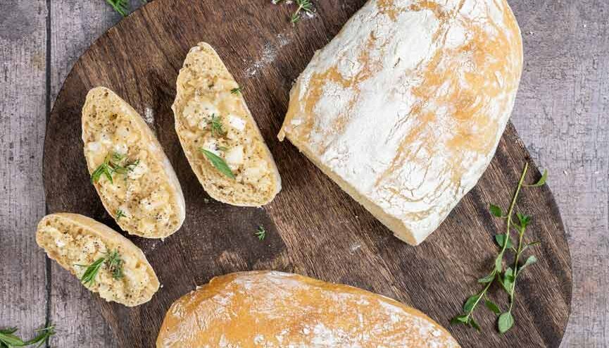 Holzbrett mit geschnittenem Brot und Kräuterbutter, garniert mit frischen Kräutern auf rustikalem Untergrund.