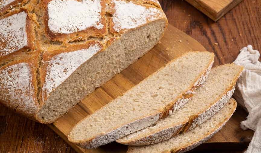 Laib rustikales Brot auf Holzbrett mit mehreren geschnittenen Scheiben, umgeben von Holzuntergrund.