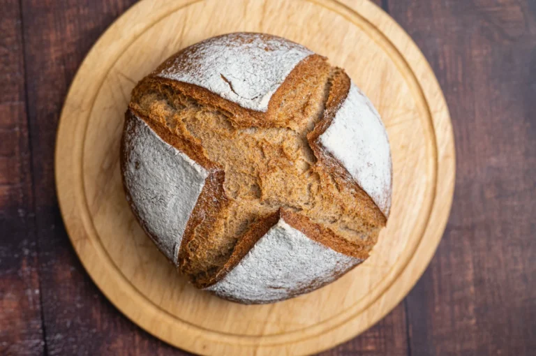 Rundes, gebackenes Brotlaib mit Mehl bestäubt auf einem Holzbrett, Draufsicht.