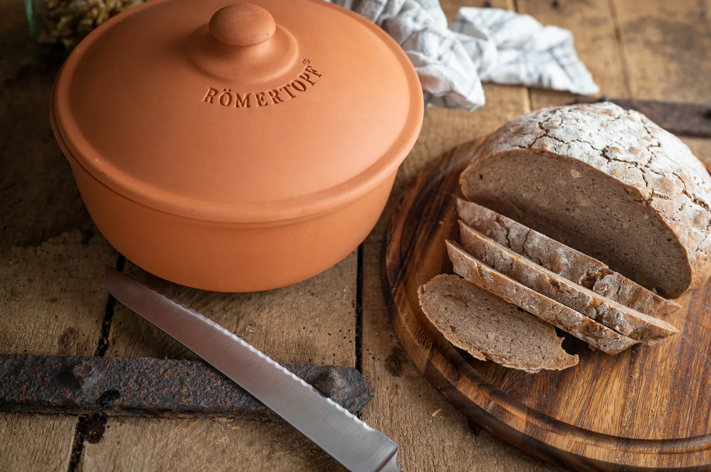 Keramiktopf und geschnittenes Brot auf einem Holzbrett neben einem Messer auf einem Holztisch.