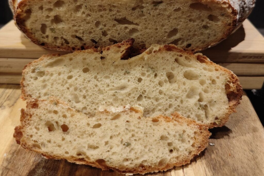 Nahaufnahme von geschnittenem Sauerteigbrot mit luftiger Krume und knuspriger Kruste auf einem Holzbrett.