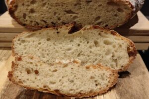 Nahaufnahme von geschnittenem Sauerteigbrot mit luftiger Krume und knuspriger Kruste auf einem Holzbrett.