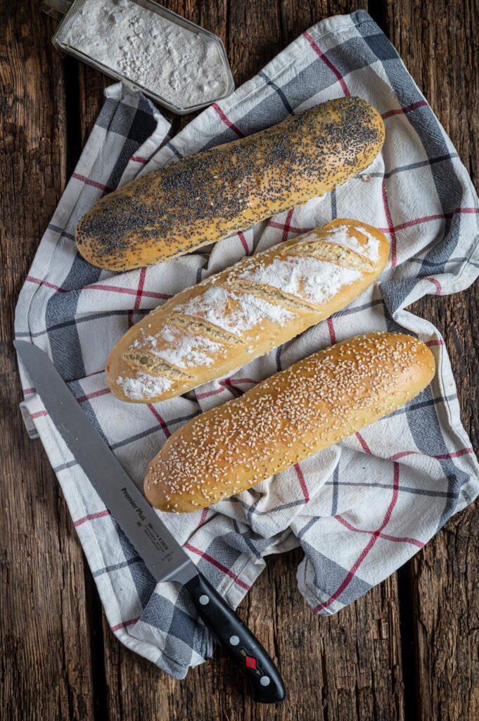 Drei Sandwich Baguettes mit Mohn, Mehl und Sesam auf einem karierten Küchentuch