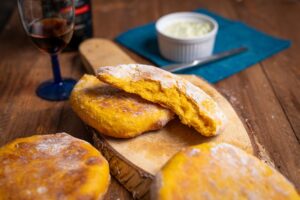 Aufgebrochenes Bolo do Caco mit gelber Süßkartoffel-Krume auf einem Holzbrett, daneben Kräuterbutter