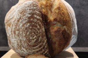 Krustiges, rundes Sauerteigbrot mit auffälligem Rillenmuster, aufgeschnitten auf einem Holzbrett vor dunklem Hintergrund.