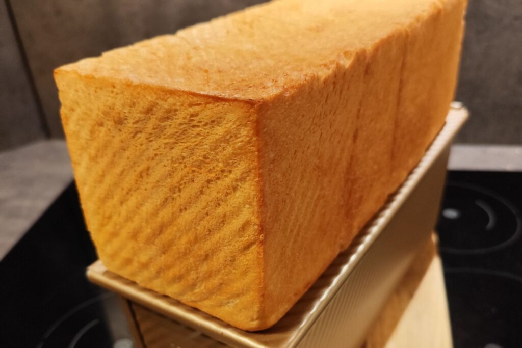 Ein quadratisches, goldbraunes Toastbrot steht in einer Metallform auf einem Herd.