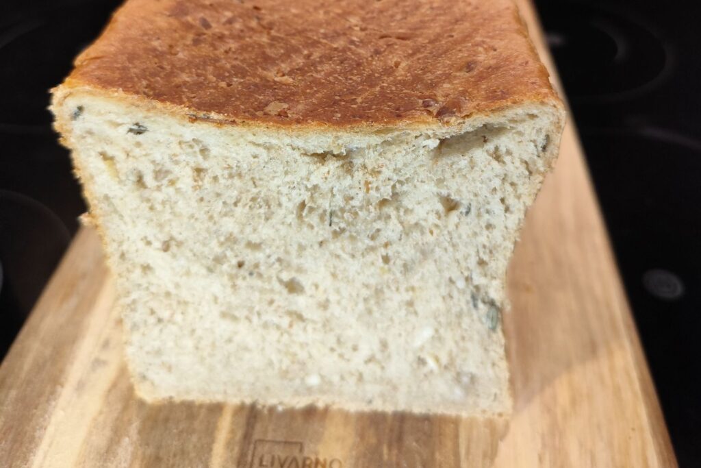 Nahaufnahme eines frisch gebackenen Brotes auf einem Holzbrett, das die saftige Krume und leicht gebräunte Kruste zeigt.