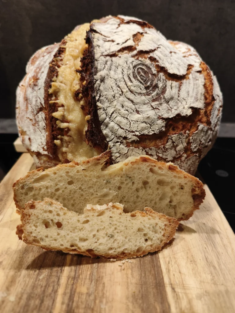 Kräftiges Sauerteigbrot mit knuspriger Kruste und einer aufgeschnittenen, luftigen Scheibe auf Holzbrett.