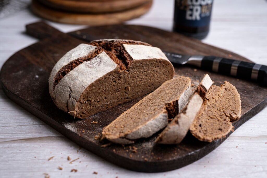 Angeschnittenes Altbier-Roggenvollkornbrot mit dunkler Krume auf Holzbrett neben einer Flasche Altbier