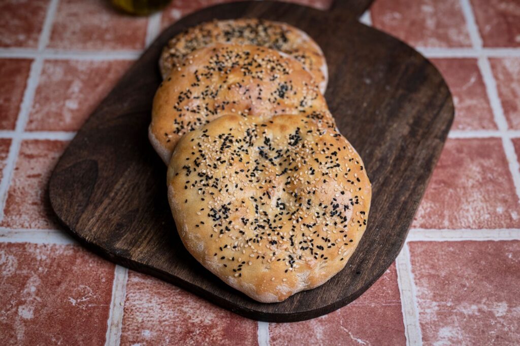 Drei selbst gebackene Dönerbrote mit Sesam und Schwarzkümmel auf Holzbrett