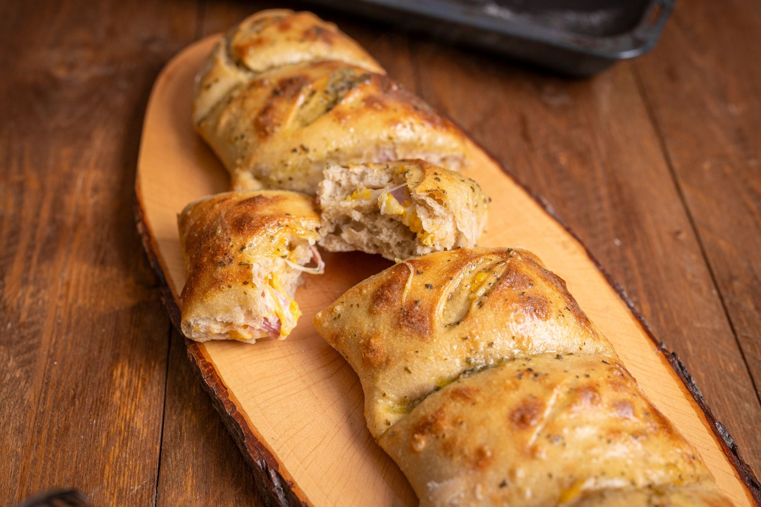 Aufgebrochenes Handbrot mit geschmolzenem Käse und Schinken auf Holzbrett