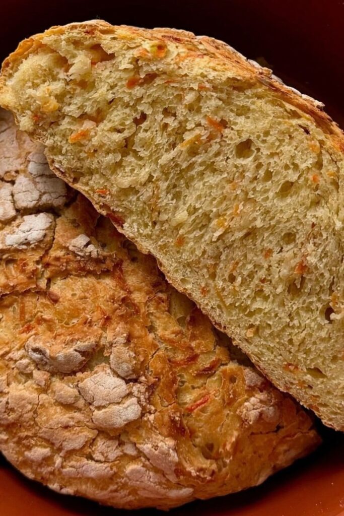 Angeschnittenes Karottenbrot mit Dinkel im Römertopf mit sichtbaren Karottenraspeln in der Krume